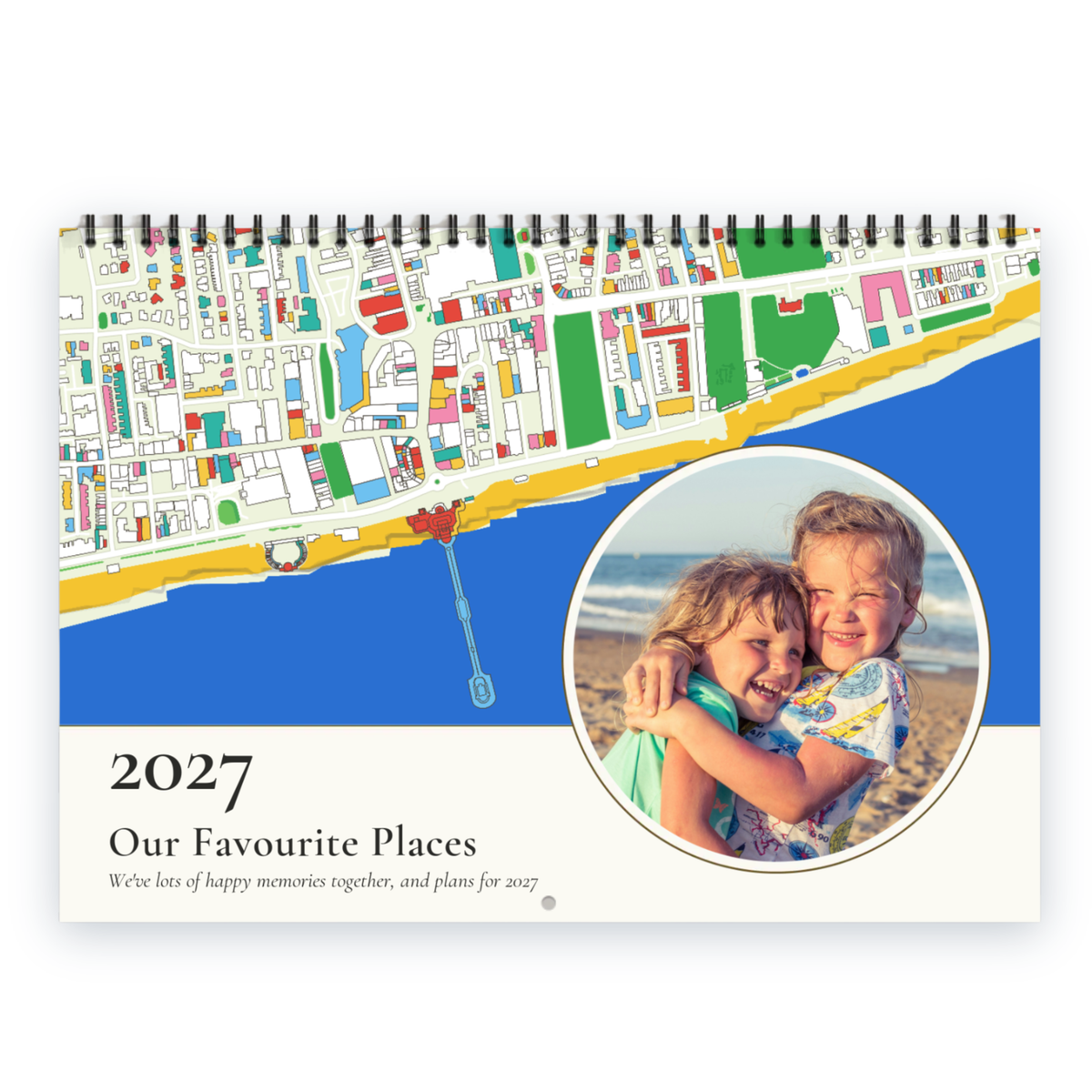 A spiral-bound 2027 personallised calendar titled 'Our Favourite Places' with a colourful coastal map illustration, a blue and white design, and a circular inset photo of two children hugging on a beach.
