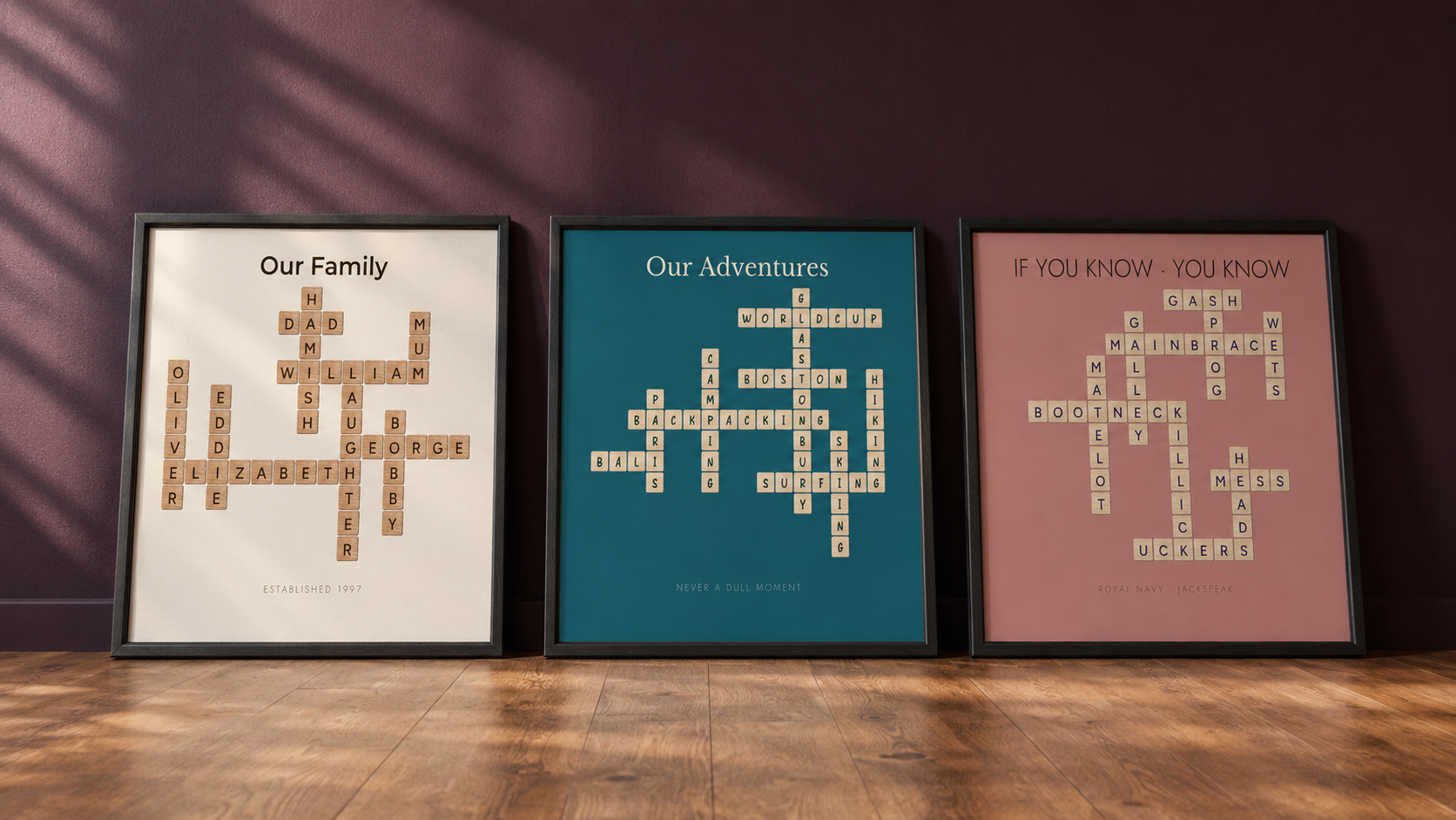 Three framed crossword-style prints on a dark wall — cream, teal, and pink backgrounds, each with names and words arranged into a crossword grid.